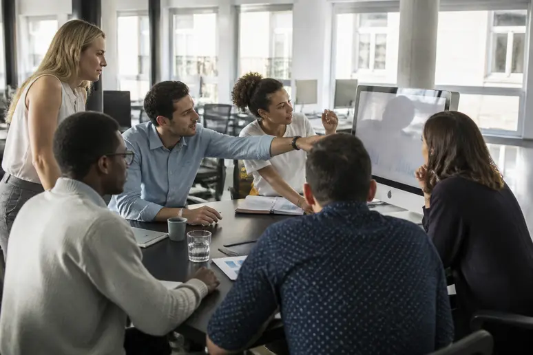 Des collègues français échangent activement autour d'un écran lors d'une session de brainstorming en milieu professionnel.