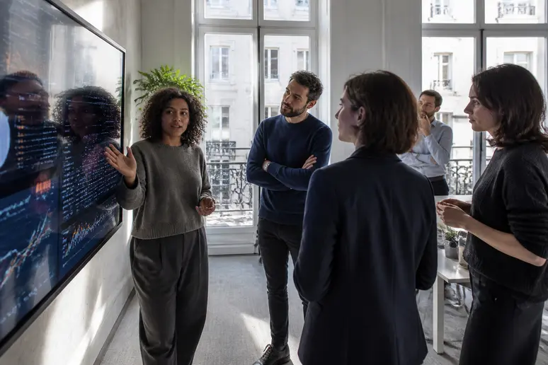Professionnels français discutant de données complexes sur un écran numérique dans un bureau parisien moderne.