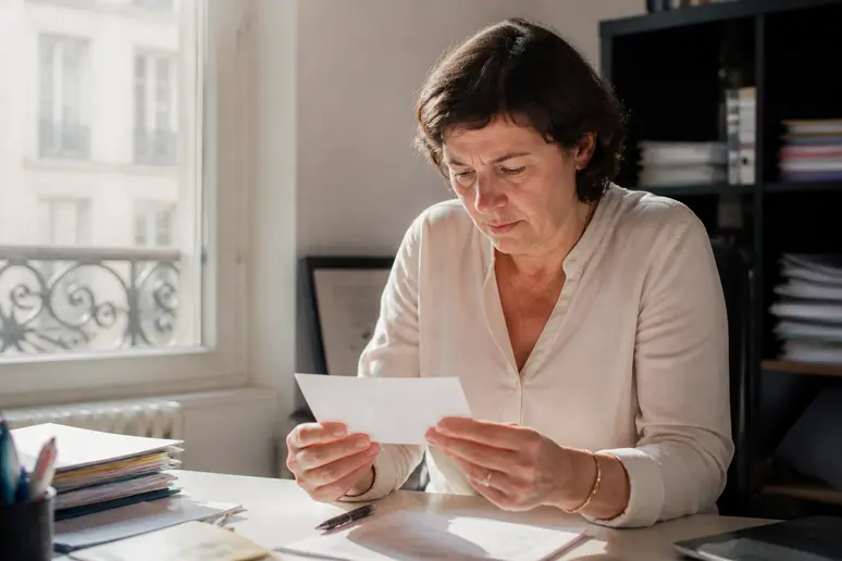 Une propriétaire de petite entreprise à Paris examine attentivement un chèque sur son bureau, concentrée sur les détails.