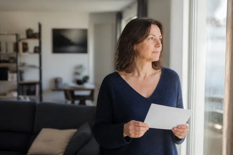 Locataire réfléchissant à une demande de travaux d'amélioration dans son appartement, tenant une lettre formelle.