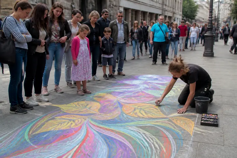 Un artiste de rue parisien réalise une œuvre éphémère au sol, captivant l'attention des passants curieux.