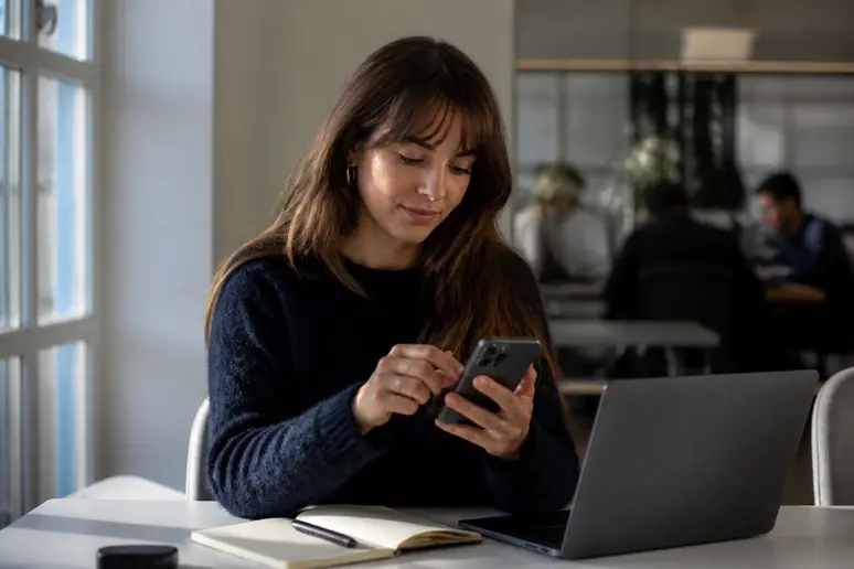 Une jeune femme configure une automatisation sur son iPhone dans un espace de coworking, illustrant la planification de SMS avant iOS 18.