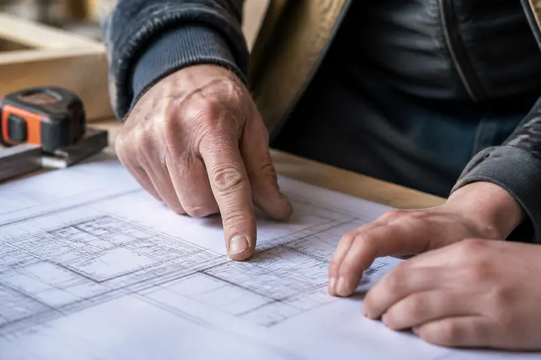 Mains expérimentées guidant des mains plus jeunes sur un plan technique pour un transfert de savoir.