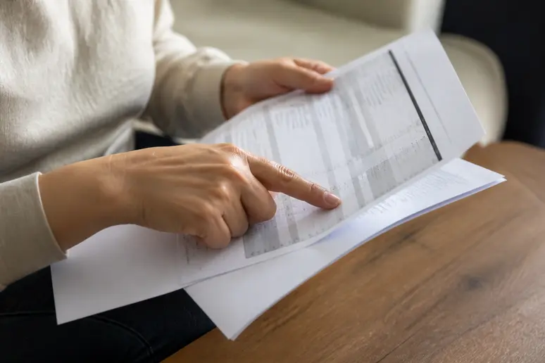 Main tenant un contrat et une fiche de paie, pointant une ligne spécifique pour vérification.