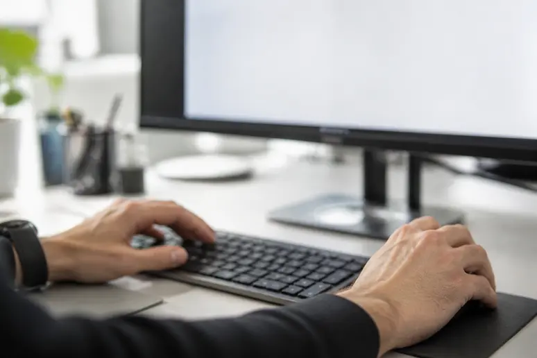 Mains d'une personne tapant sur un clavier, préparant un envoi d'e-mails, avec une interface logicielle visible.