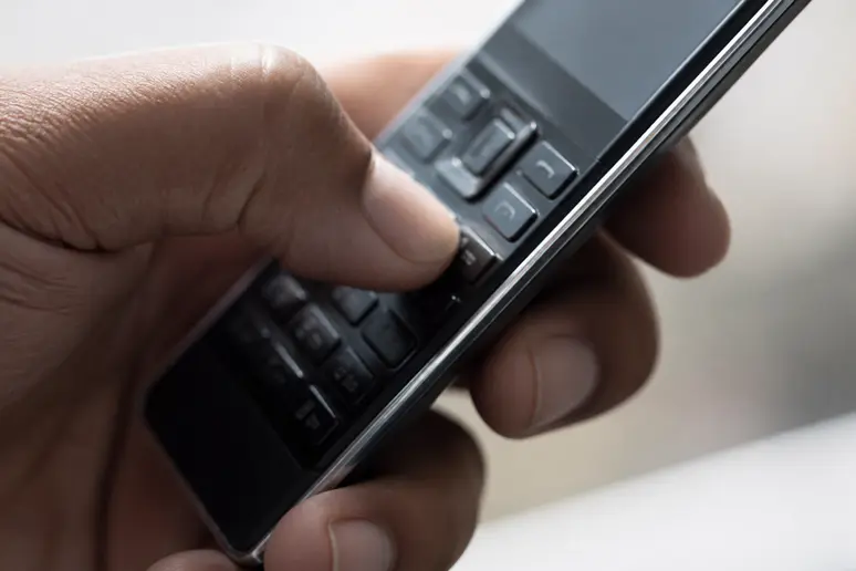Gros plan sur un pouce composant une séquence de chiffres sur le clavier d'un téléphone mobile.
