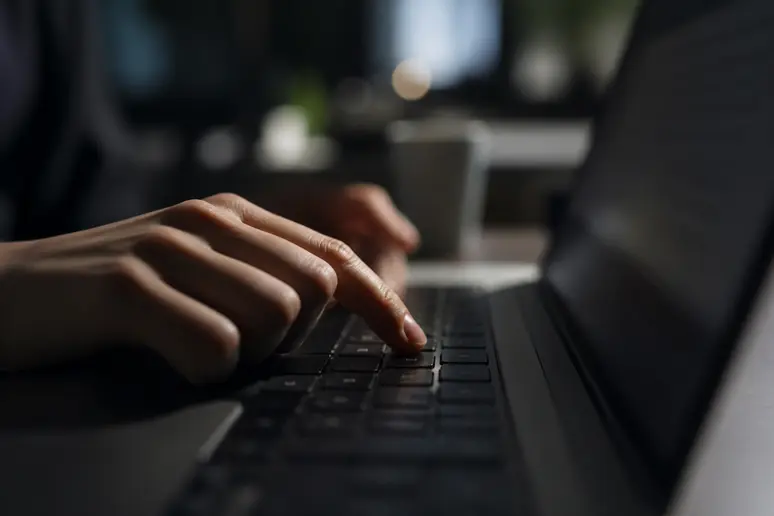 Main hésitant à cliquer sur une pièce jointe d'email suspecte sur un écran d'ordinateur.