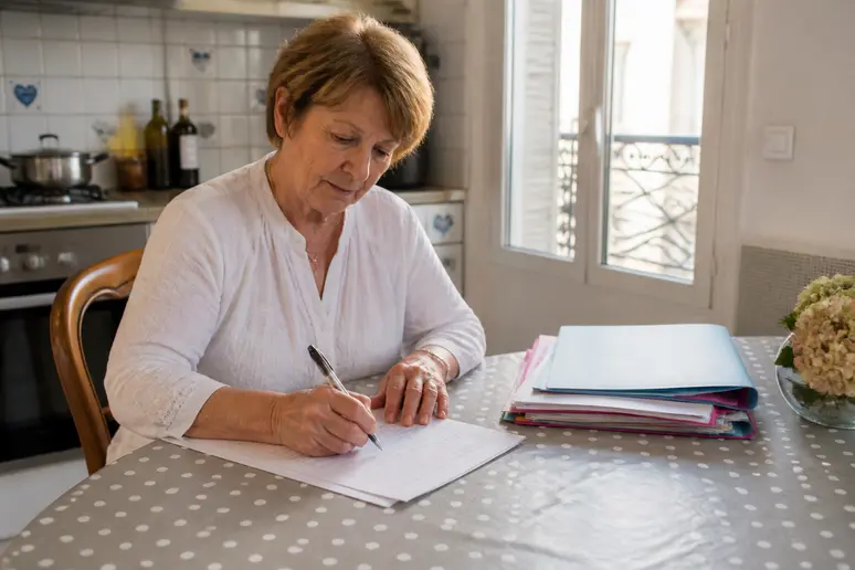 Une senior remplissant un formulaire pour des aides et services à domicile seniors.