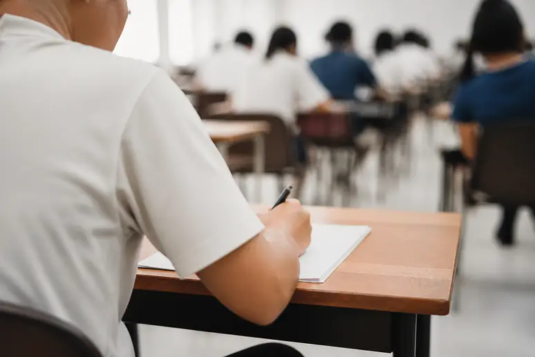 Candidat remplissant un formulaire d'évaluation sur une table dans une salle d'examen professionnelle